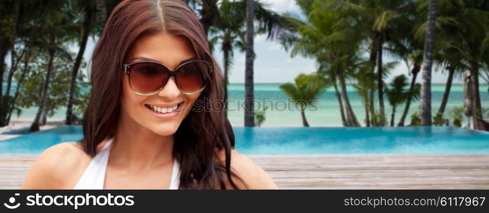 summer vacation, tourism, travel, holidays and people concept -face of smiling young woman with sunglasses over tropical beach with palms and swimming pool background