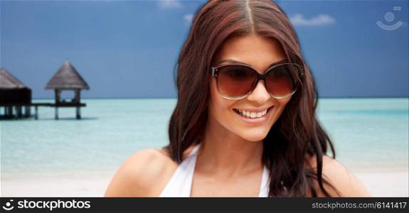 summer vacation, tourism, travel, holidays and people concept -face of smiling young woman with sunglasses over bungalow on beach background