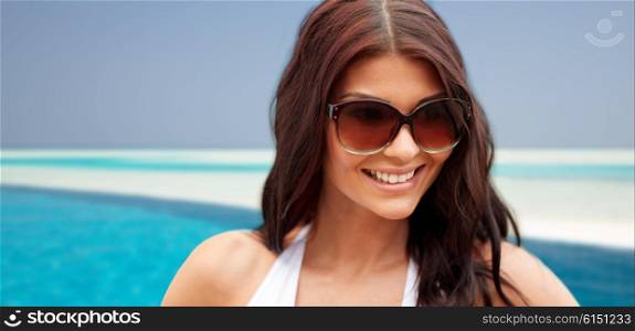 summer vacation, tourism, travel, holidays and people concept -face of smiling young woman with sunglasses over beach and swimming pool background