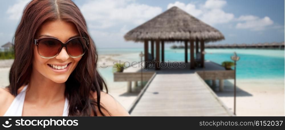summer vacation, tourism, travel, holidays and people concept -face of smiling young woman with sunglasses over bungalow on beach background