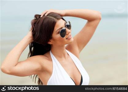 summer vacation, tourism, travel, holidays and people concept -face of smiling young woman in swimsuit with sunglasses on beach