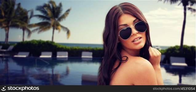 summer vacation, tourism, travel, holidays and people concept -face of young woman with sunglasses over resort beach with palms and swimming pool background
