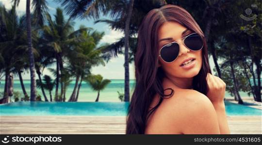 summer vacation, tourism, travel, holidays and people concept -face of young woman with sunglasses over tropical beach with palms and swimming pool background