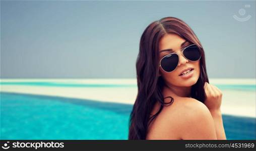 summer vacation, tourism, travel, holidays and people concept -face of young woman with sunglasses over beach and swimming pool background