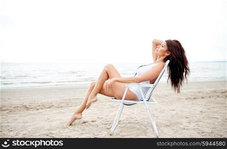 summer vacation, tourism, travel, holidays and people concept - happy young woman sunbathing in lounge or folding chair on beach