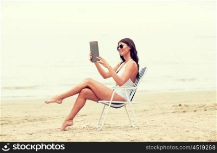 summer vacation, tourism, travel, holidays and people concept - smiling young woman with tablet pc computer sunbathing in lounge or folding chair on beach