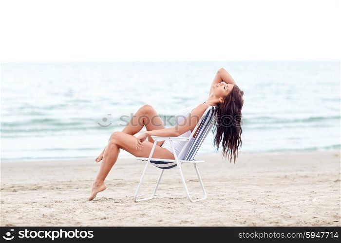 summer vacation, tourism, travel, holidays and people concept - smiling young woman sunbathing in lounge or folding chair on beach