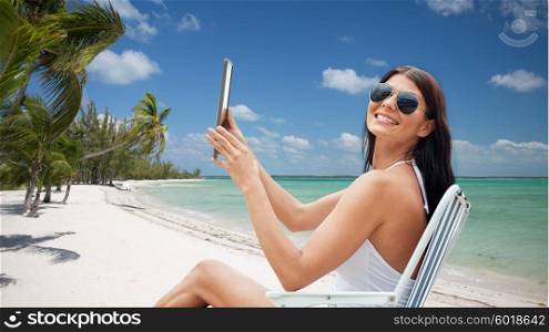 summer vacation, tourism, travel, holidays and people concept - smiling young woman with tablet pc computer sunbathing in lounge or folding chair over tropical beach with palms background
