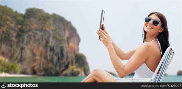 summer vacation, tourism, travel, holidays and people concept - smiling young woman with tablet pc computer sunbathing in lounge or folding chair over rock on bali beach background