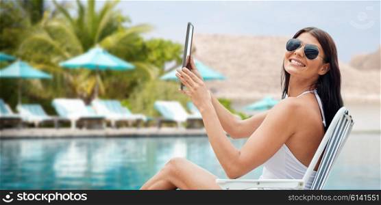 summer vacation, tourism, travel, holidays and people concept - smiling young woman with tablet pc computer sunbathing in lounge or folding chair over beach and swimming pool background