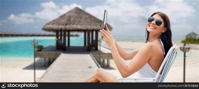 summer vacation, tourism, travel, holidays and people concept - smiling young woman with tablet pc computer sunbathing in lounge or folding chair over bungalow on beach background