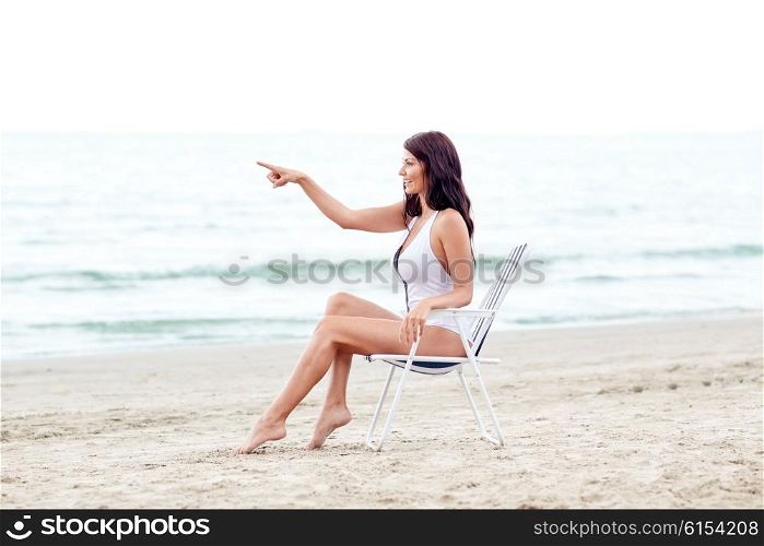 summer vacation, tourism, travel, holidays and people concept - smiling young woman sunbathing in lounge or folding chair pointing finger on beach