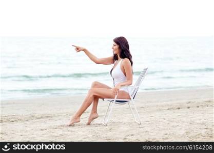 summer vacation, tourism, travel, holidays and people concept - smiling young woman sunbathing in lounge or folding chair pointing finger on beach