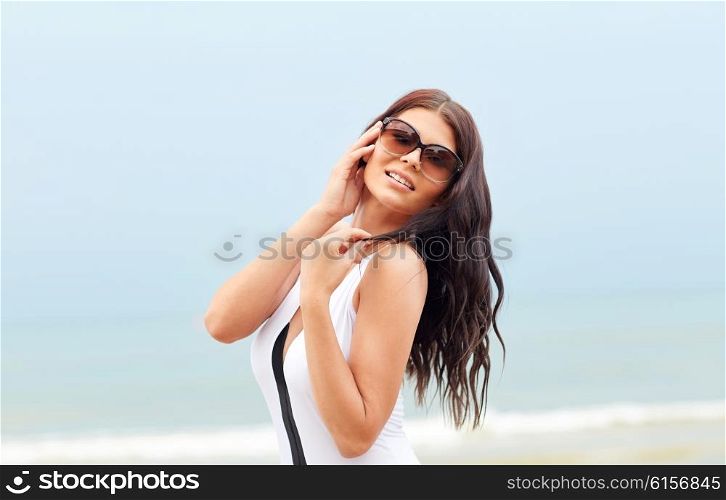 summer vacation, tourism, travel, holidays and people concept -smiling young woman in swimsuit with sunglasses on beach