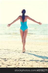 summer vacation, tourism, travel, holidays and people concept -young woman in swimsuit posing on beach from back
