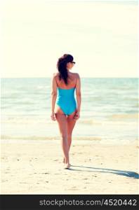 summer vacation, tourism, travel, holidays and people concept -young woman in swimsuit walking on beach from back