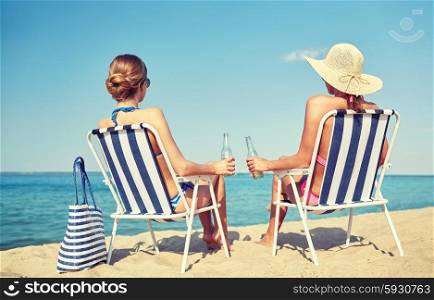 summer vacation, travel and people concept - happy women drinking beer and sunbathing in lounges on beach