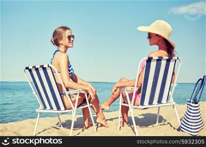 summer vacation, travel and people concept - happy women sunbathing in lounges on beach