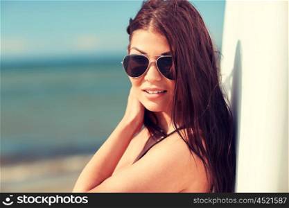summer vacation, travel, surfing, water sport and people concept - young woman in sunglasses with surfboard on beach