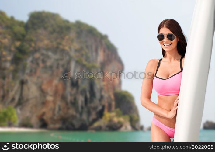 summer vacation, travel, surfing, water sport and people concept - young woman in swimsuit with surfboard over rock on bali beach background