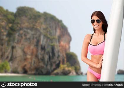 summer vacation, travel, surfing, water sport and people concept - young woman in swimsuit with surfboard over rock on bali beach background