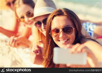 summer vacation, travel, technology and people concept - close up of smiling women in sunglasses and hats making selfie with smartphone on beach