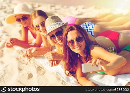summer vacation, travel, technology and people concept - group of smiling women in sunglasses and hats making selfie with smartphone on beach