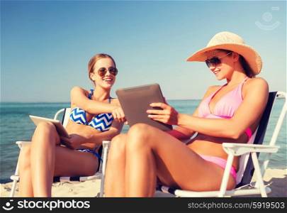 summer vacation, travel, technology and people concept - smiling women with tablet pc computers sunbathing in lounge on beach