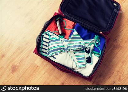 summer vacation, travel, tourism and objects concept - close up of travel bag with beach clothes, sunglasses and sunscreen. close up of travel bag with beach clothes