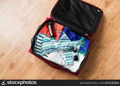 summer vacation, travel, tourism and objects concept - close up of travel bag with beach clothes, sunglasses and sunscreen