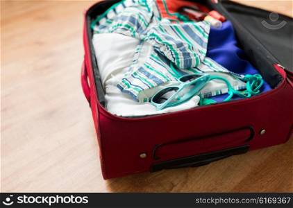 summer vacation, travel, tourism and objects concept - close up of travel bag with beach clothes, sunglasses and sunscreen
