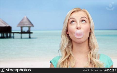 summer vacation, travel, tourism and people concept - happy young woman or teenage girl chewing gum over beach on touristic resort background