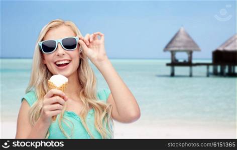 summer vacation, travel, tourism, junk food and people concept - young woman or teenage girl in sunglasses eating ice cream over beach on touristic resort background