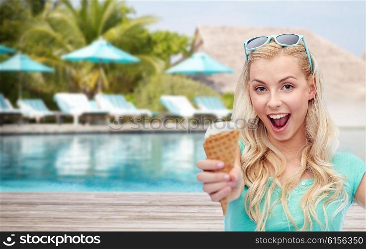 summer vacation, travel, tourism, junk food and people concept - young woman or teenage girl in sunglasses eating ice cream over beach on touristic resort background