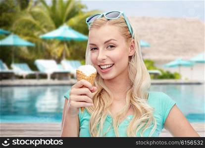 summer vacation, travel, tourism, junk food and people concept - young woman or teenage girl in sunglasses eating ice cream over pool on resort beach background