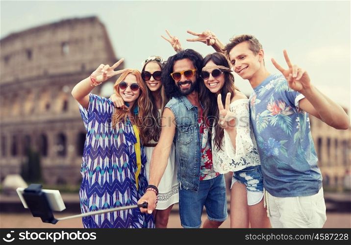 summer vacation, travel, tourism, technology and people concept - smiling young hippie friends taking picture by smartphone selfie stick over coliseum background
