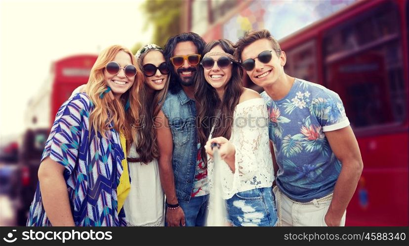 summer vacation, travel, tourism, technology and people concept - smiling young hippie friends taking picture by smartphone selfie stick over london city street background