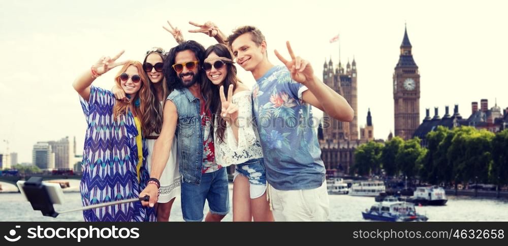 summer vacation, travel, tourism, technology and people concept - smiling young hippie friends taking picture by smartphone selfie stick over london city and big ben tower background