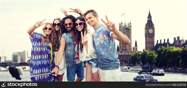 summer vacation, travel, tourism, technology and people concept - smiling young hippie friends taking picture by smartphone selfie stick over london city and big ben tower background