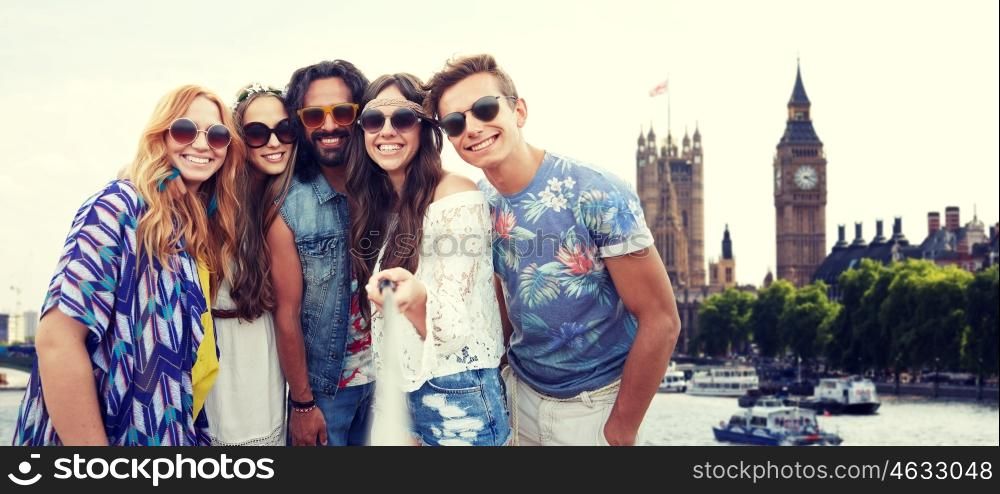 summer vacation, travel, tourism, technology and people concept - smiling young hippie friends taking picture by smartphone selfie stick over big ben tower in london city background