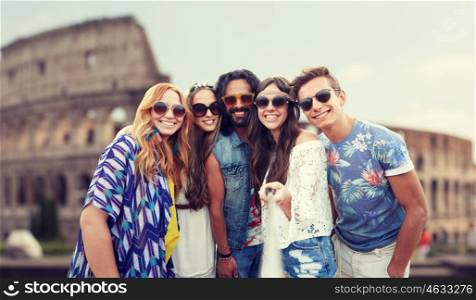 summer vacation, travel, tourism, technology and people concept - smiling young hippie friends taking picture by smartphone selfie stick over coliseum in rome background