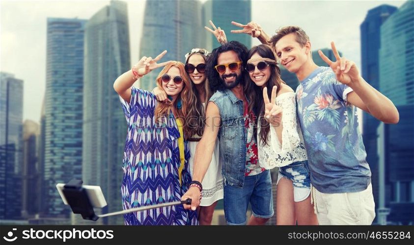 summer vacation, travel, tourism, technology and people concept - smiling young hippie friends taking picture by smartphone selfie stick over singapore city street background