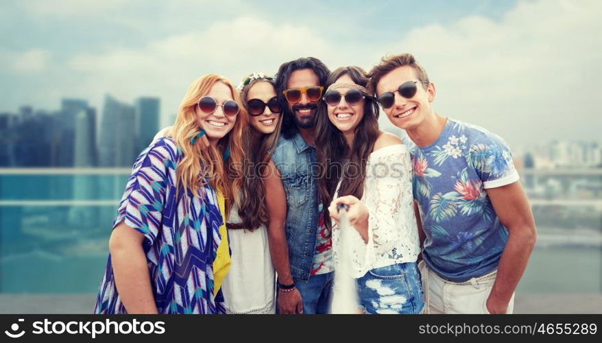 summer vacation, travel, tourism, technology and people concept - smiling young hippie friends taking picture by smartphone selfie stick over singapore city background