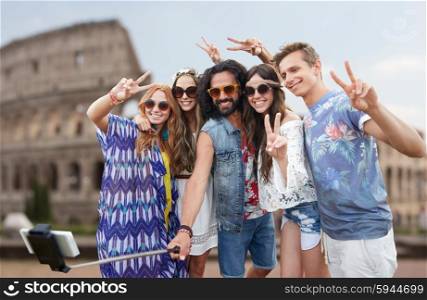 summer vacation, travel, tourism, technology and people concept - smiling young hippie friends taking picture by smartphone selfie stick over coliseum background