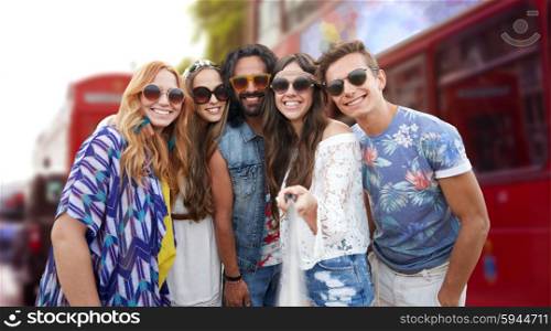 summer vacation, travel, tourism, technology and people concept - smiling young hippie friends taking picture by smartphone selfie stick over london city street background