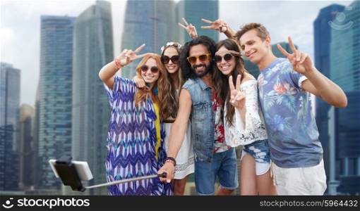 summer vacation, travel, tourism, technology and people concept - smiling young hippie friends taking picture by smartphone selfie stick over singapore city street background