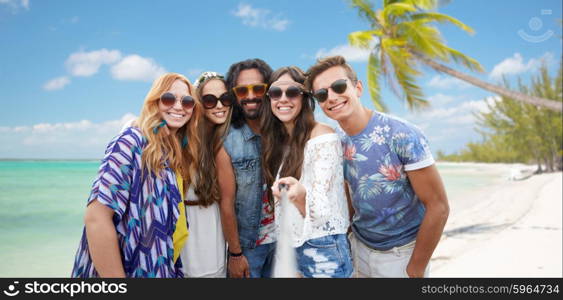 summer vacation, travel, tourism, technology and people concept - smiling young hippie friends taking picture by smartphone selfie stick over beach background