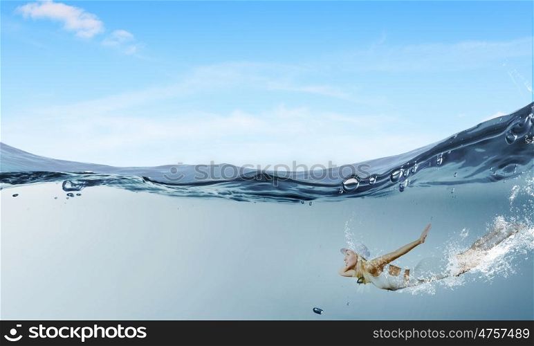 Summer vacation. Young pretty girl in hat and dress swimming under water
