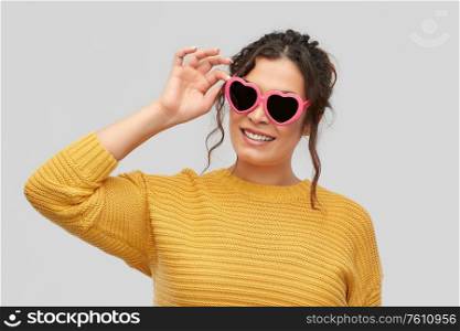 summer, valentine&rsquo;s day and eyewear concept - portrait of happy smiling young woman with pierced nose in pink heart-shaped sunglasses over grey background. smiling young woman in heart-shaped sunglasses