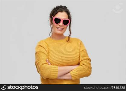 summer, valentine&rsquo;s day and eyewear concept - portrait of happy smiling young woman with pierced nose in pink heart-shaped sunglasses over grey background. smiling young woman in heart-shaped sunglasses